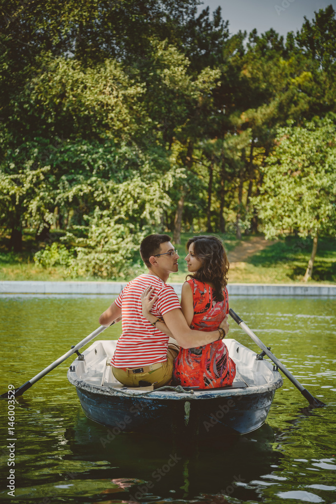 Young beautiful happy loving couple rowing a small boat on a lake. A fun date in nature. Couple hugging in a boat. Young beautiful happy loving couple rowing a small boat on a lake. A fun date in nature. Couple hugging in a boat.