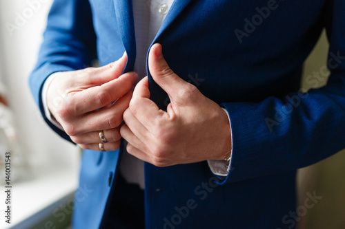 Businessman corrects buttons on his jacket, hands close-up, dressing, man's style, correcting sleeves, preparing for the wedding