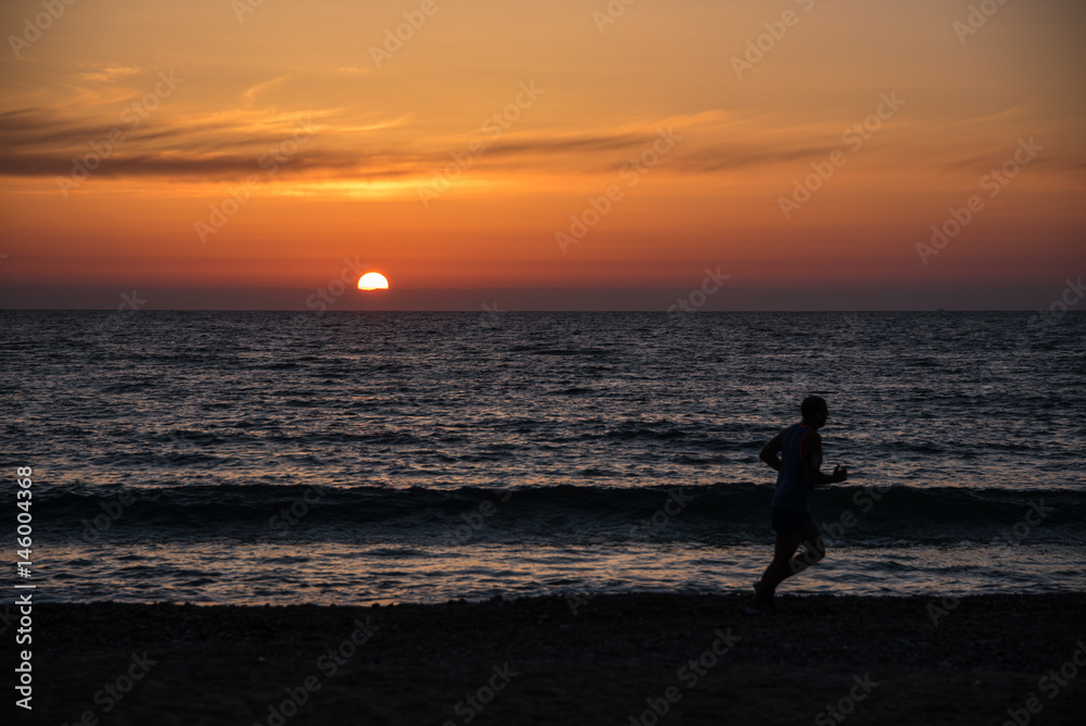 Jogger at the beach in front of a colourful sunset