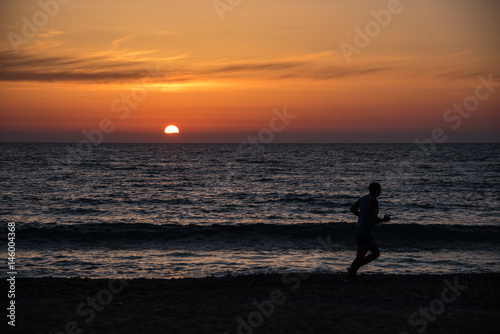 Jogger at the beach in front of a colourful sunset