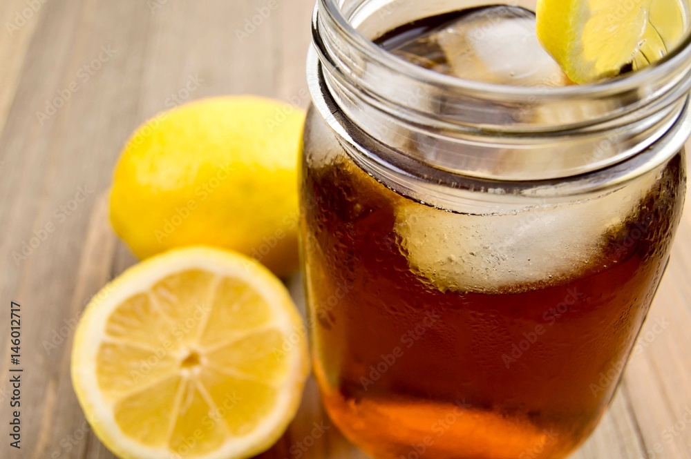 Mason jar of Iced tea with lemon on a wooden surface Mason jar of Iced tea with lemon on a wooden surface