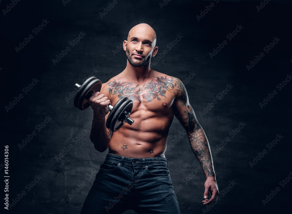 Positive shaved head shirtless male dressed in a jeans holds the dumbbell. Positive shaved head shirtless male dressed in a jeans holds the dumbbell.