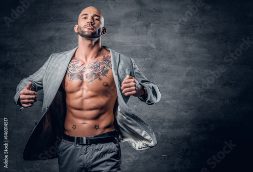 Shaved head tattooed male dressed in a grey jacket on a naked torso. © Fxquadro