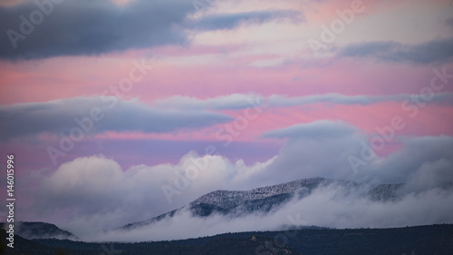 Snow-dusted mountains surrounded in clouds at sunset