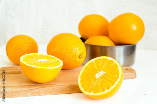 Fresh oranges,cutting board and metall bowl on white wooden background. Selective focus. Wellness setting. Health concept.