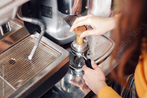 small business, people and service concept - woman or waiter in apron with holder and tamper preparing coffee at coffee shop photo