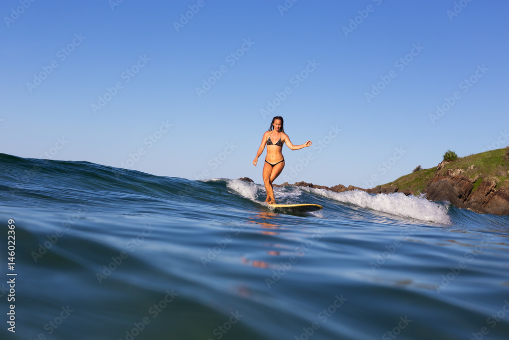 A woman elegantly cross-steps on a longboard at an isolated surf break in Australia.