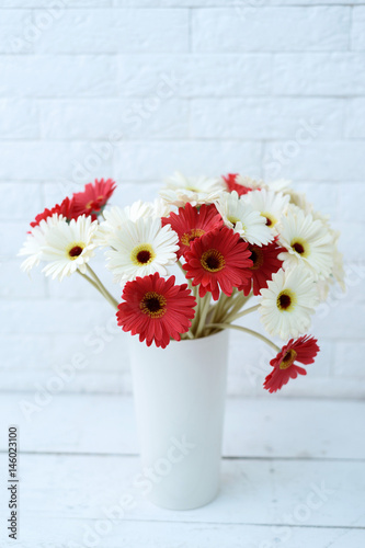 White and red gerberas in white vase near white brick wall