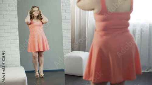 Joyful girl looking at her curvy shape in short dress and rejoicing in her image