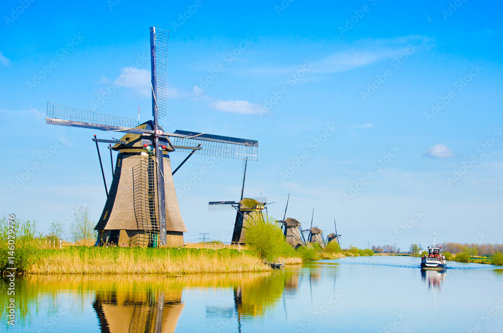 The charming landscape with windmills and boat on river in Kinderdijk, Netherlands, Europe against a background of cloudy sky reflection in the water.