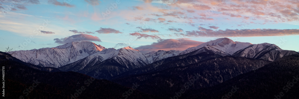 Mountain winter landscape at sunset with lenticular clouds over high snow-capped peaks. Caucasus. Russia. The Caucasian reserve. View from Mount Kazachya
