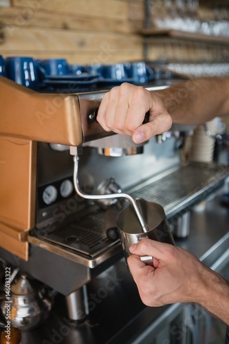 Close-up of waiter hands pouring milk in jug from coffee machine