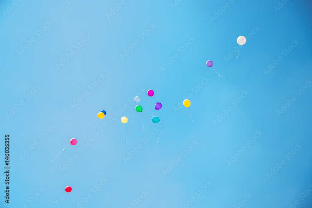 Many balloons of different colors are pumped with helium flying up into a blue sky in summer