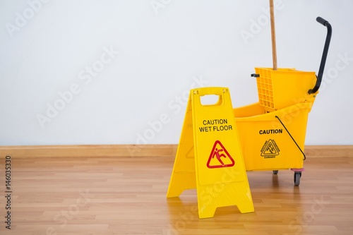 Yellow sigh boad with mop bucket on floor against wall photo