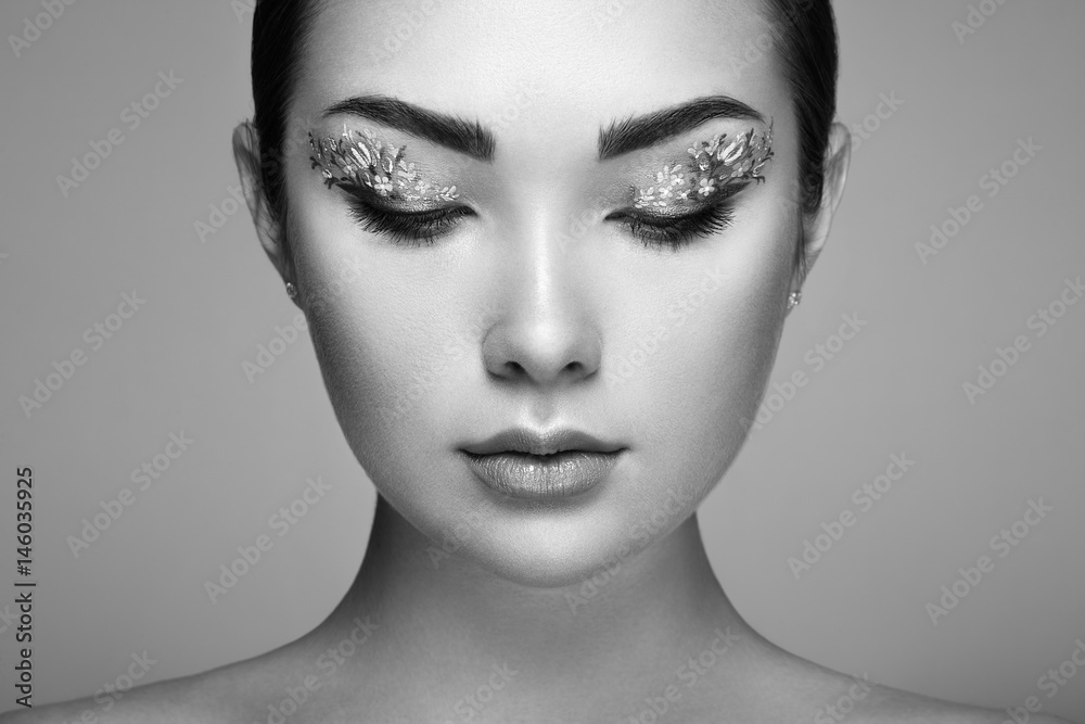 Fototapeta premium Young beautiful woman with flower makeup eyes. Spring makeup. Beauty fashion. Eyelashes. Cosmetic Eyeshadow. Make-up detail. Girl on green background. Black and White photo