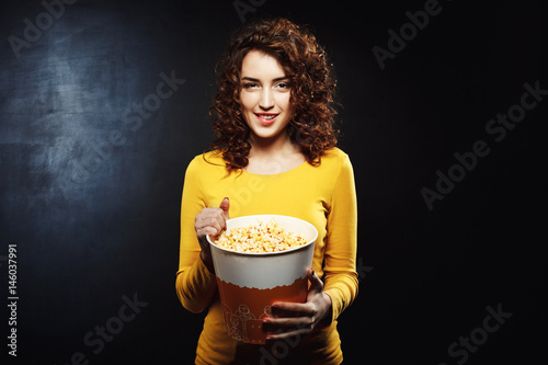 Nice young woman playing on camera with popcorn looking straight photo