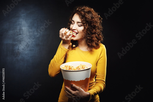 Hungry woman eats handful of popcorn while waiting for movie photo