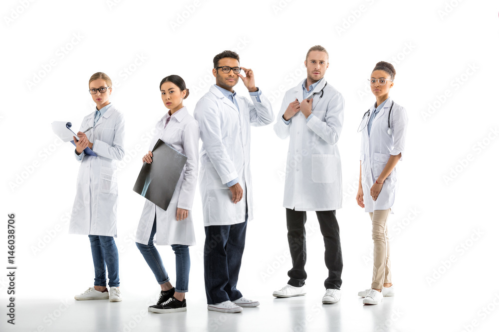 Group of young confident professional doctors in white coats standing isolated on white