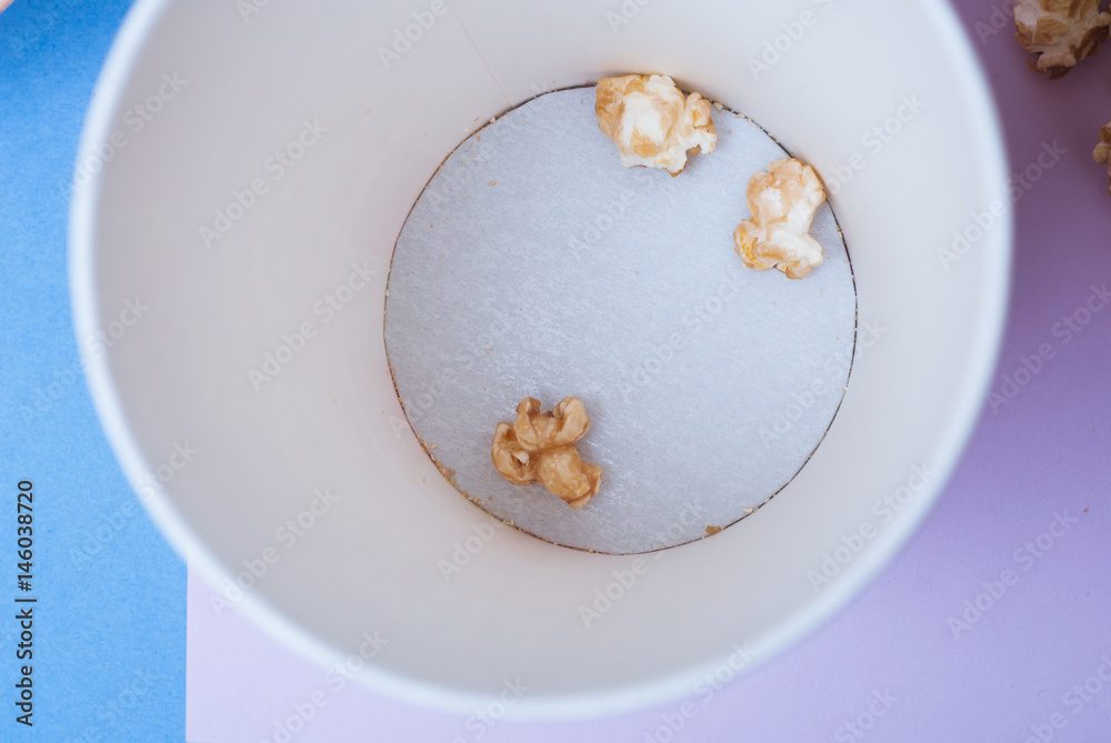 A top view of a Cup with the remnants of the popcorn on the bottom, purple background, paper Cup, A top view of a Cup with the remnants of the popcorn on the bottom, purple background, paper Cup,