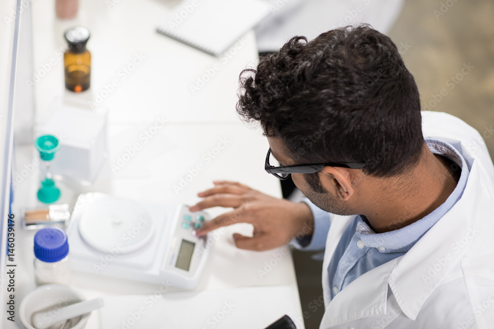 High angle view of young scientist working with electronic scales in research laboratory High angle view of young scientist working with electronic scales in research laboratory