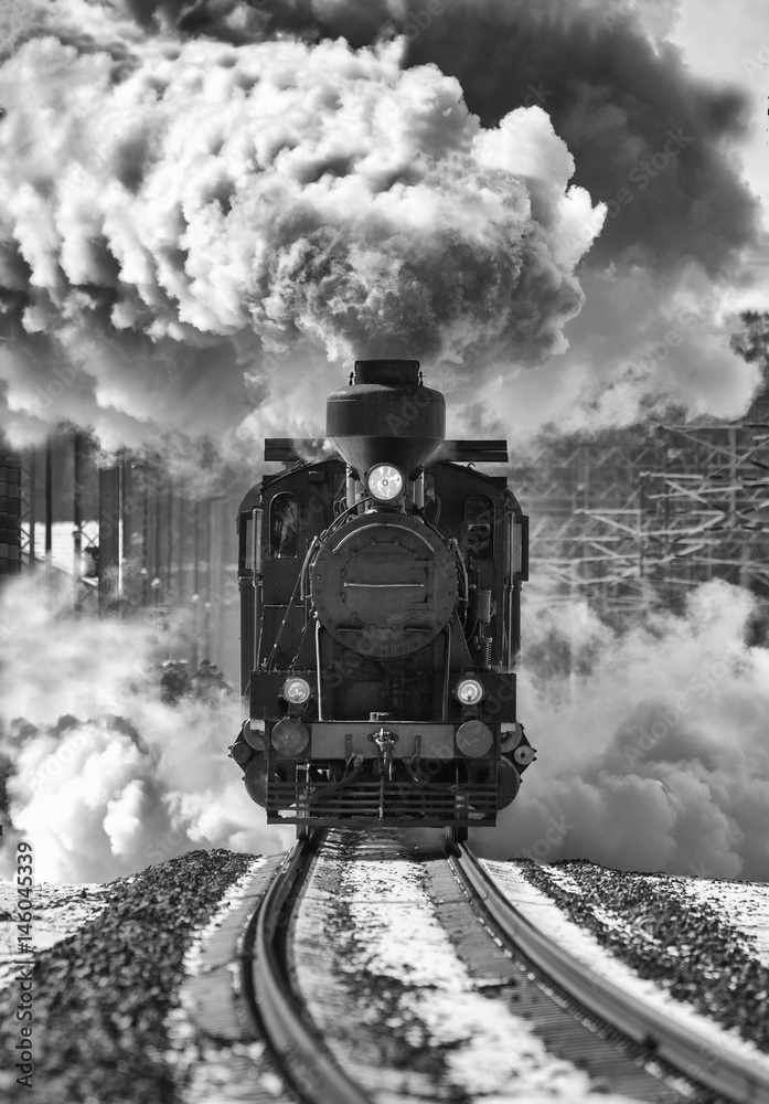 Naklejka premium Historyczna lokomotywa opuszczająca stację. Pociąg retro na szynach. Niebo pełne dymu. Obraz czarno-biały.