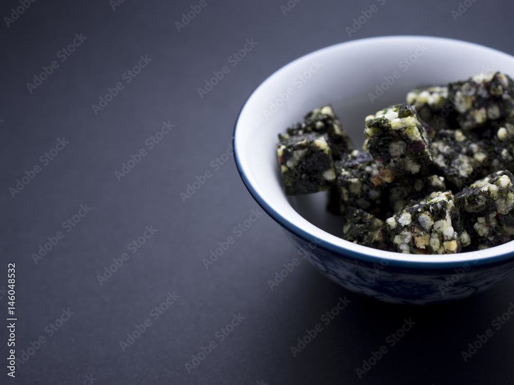 Seaweed snacks in cubes with cranberries and honey placed in Chinese bowl isolated on black background Seaweed snacks in cubes with cranberries and honey placed in Chinese bowl isolated on black background
