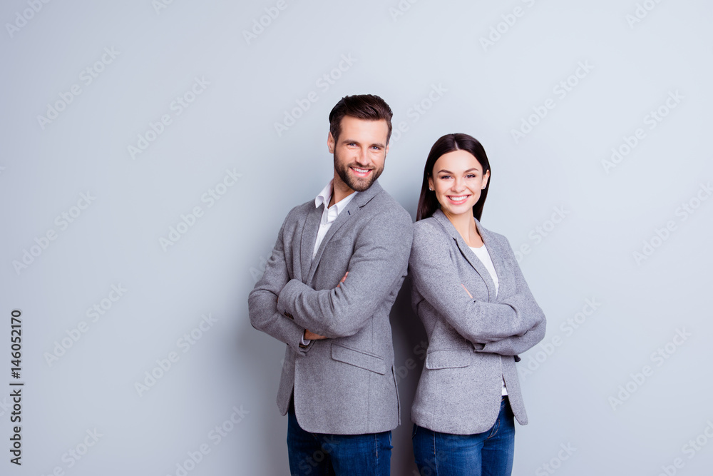 Concept of partnership in business. Young man and woman standing back-to-back with crossed hands against gray background Concept of partnership in business. Young man and woman standing back-to-back with crossed hands against gray background