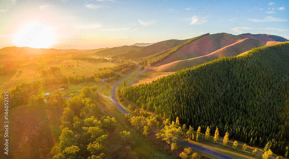 Aerial panorama of sunset over countryside - winding road, forested hills and golden colors