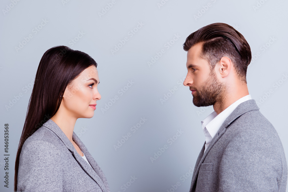 Concept of confrontation in business. Close up photo of two young serious confident people standing face-to-face to each other Concept of confrontation in business. Close up photo of two young serious confident people standing face-to-face to each other