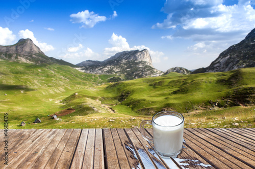 Mug of milk on a wooden table in the mountains. View of the small farm.