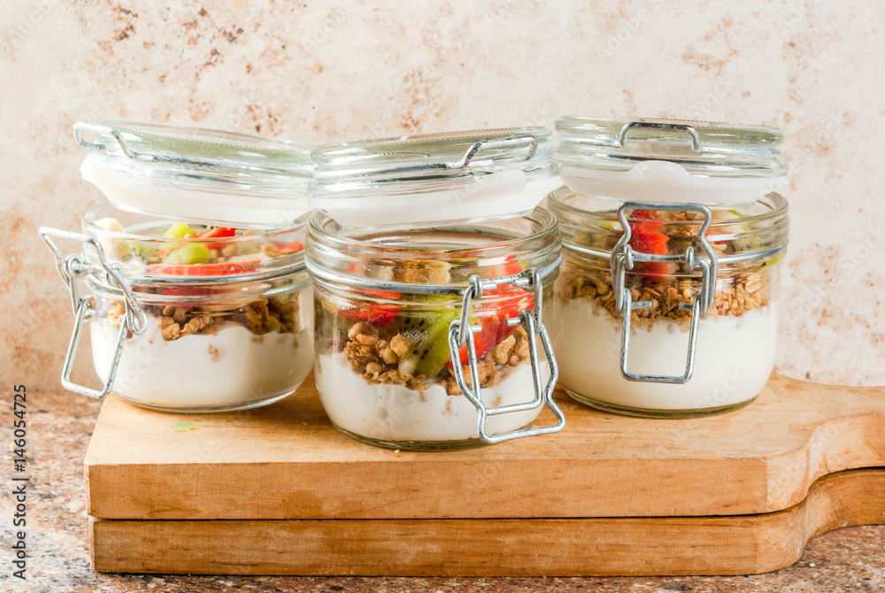 Healthy breakfast. Diet. Overnight oatmeal in a can, muesli. Yogurt with homemade granola and organic fruits - kiwi, banana, strawberry. On the stone table. With ingredients and spoons. Healthy breakfast. Diet. Overnight oatmeal in a can, muesli. Yogurt with homemade granola and organic fruits - kiwi, banana, strawberry. On the stone table. With ingredients and spoons.