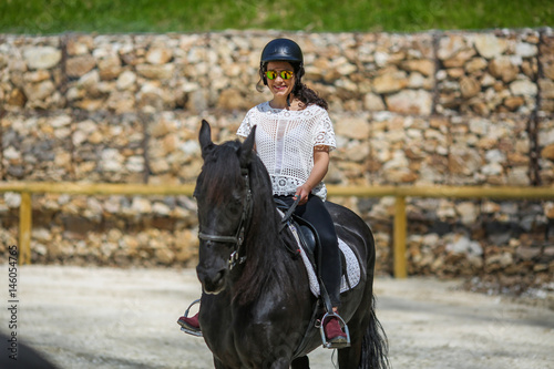 Lovely young brunette with sunglasses, riding a horse