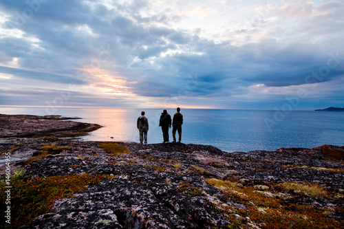 group of friends of travelers stands together in the background of the sunset and the Barents Sea. The concept of a trip to the ends of the earth, Teriberka, Kola Peninsula, Russia photo