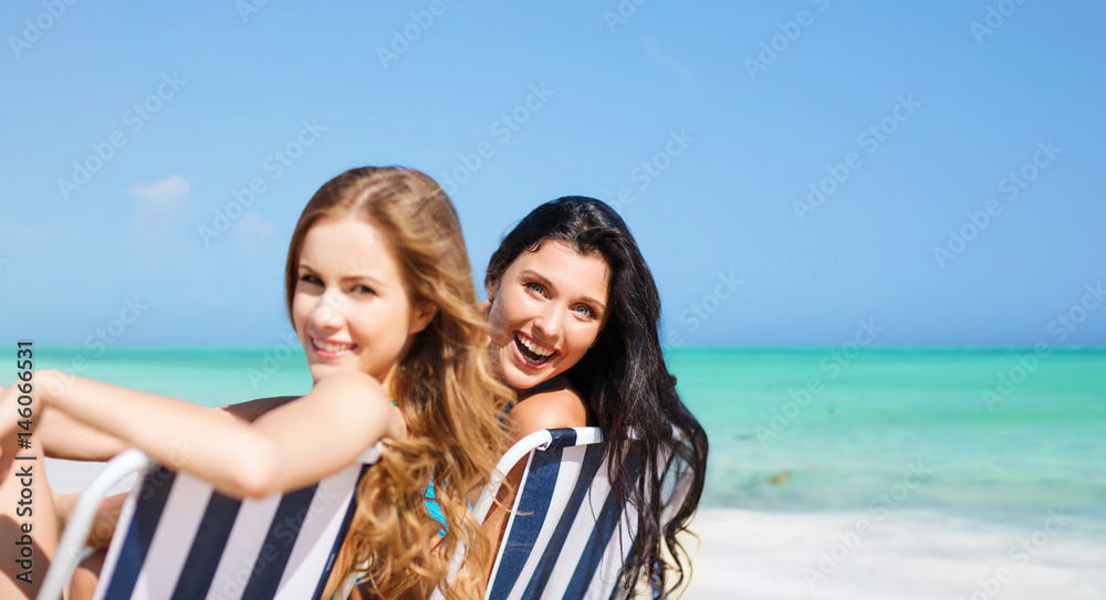 happy women sunbathing on chairs over summer beach