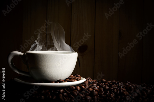Steaming coffee cup put on coffee beans on wood background.
