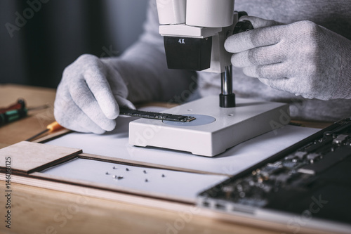 Detail image of technician examining random access memory with microscope at electronics store
