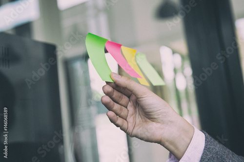 business person hand holding blank sticky paper note on window in office