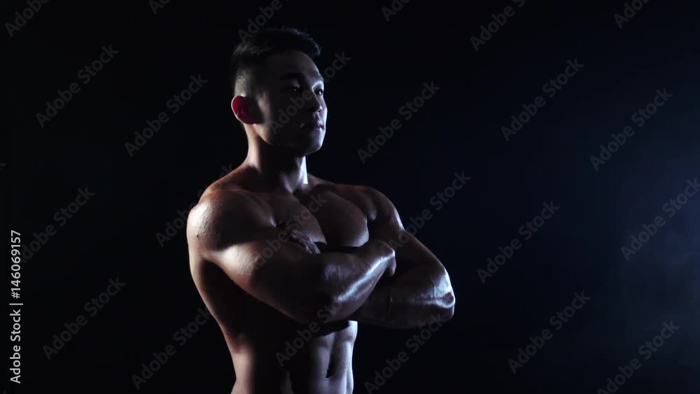 Asian bodybuilder demonstrates the inflated body, he is strong. Black background. Slow motion Asian bodybuilder demonstrates the inflated body, he is strong. Black background. Slow motion