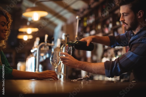 Male bar tender pouring wine in glasses