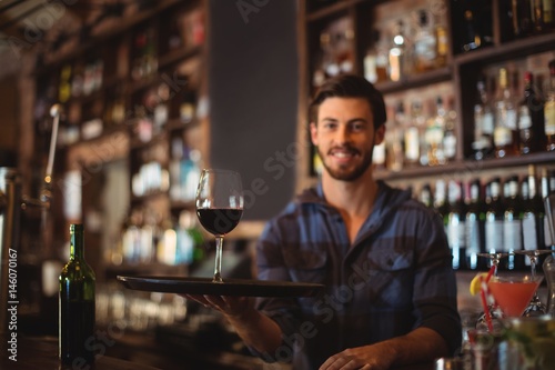 Portrait of bar tender holding a tray with glass of red wine
