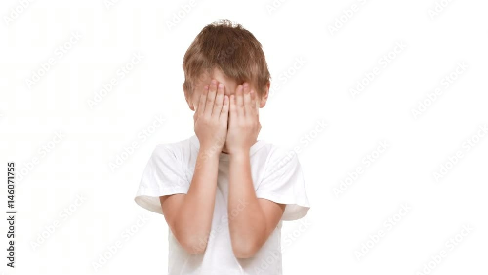 Smiling elmentary-school aged boy closing eyes with hands and laughing standing on white background Smiling elmentary-school aged boy closing eyes with hands and laughing standing on white background