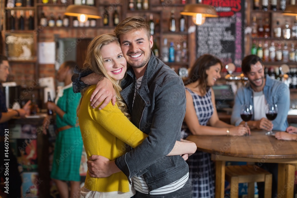 Smiling young couple hugging in pub