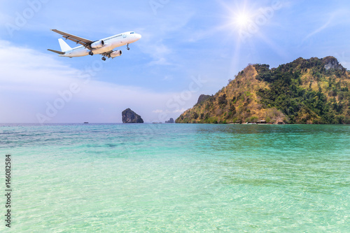 passenger airplane landing above small island in blue sea and tropical beach on blue sky with sunlight. 