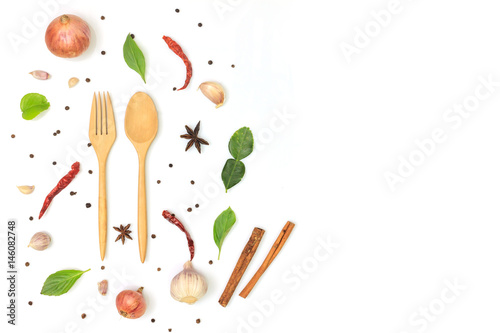  wooden spoon and fork on white background, decorate with dried chilli, garlic, onion, cinnamon, black pepper, basil leaf, lime leaf and star anise in top view. copy space