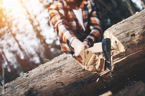 Strong logger in a plaid shirt chopping a big tree. Wood chips fly apart photo