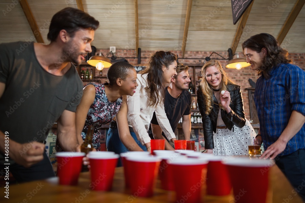 Happy friends playing beer pong game in bar Happy friends playing beer pong game in bar