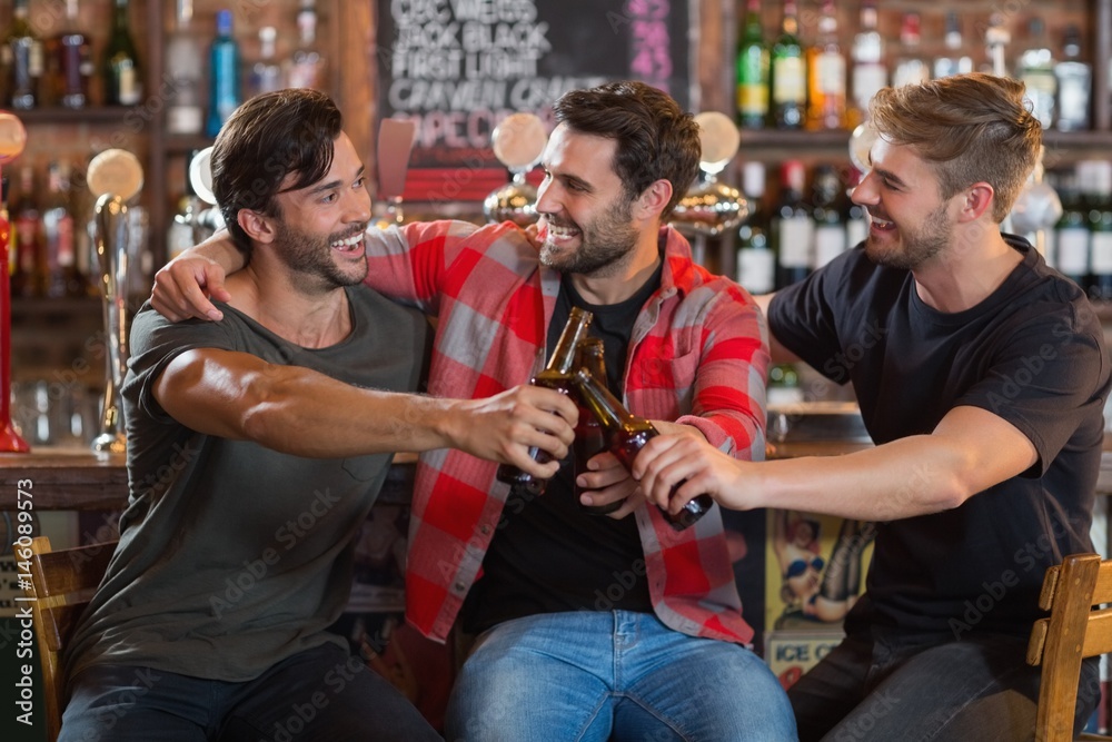Happy young male friends toasting beer bottles in bar