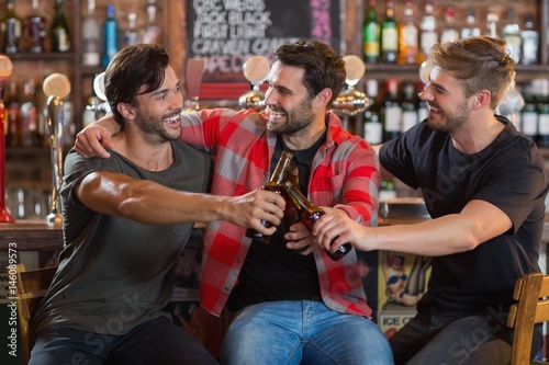 Happy young male friends toasting beer bottles in bar