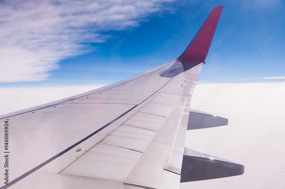 Airplane wing during flying above sea cloud with blue sky