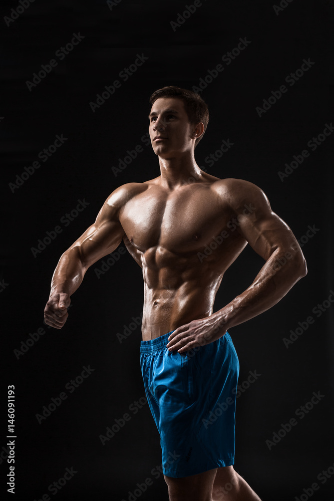 Muscular and fit young bodybuilder fitness male model posing over black background.